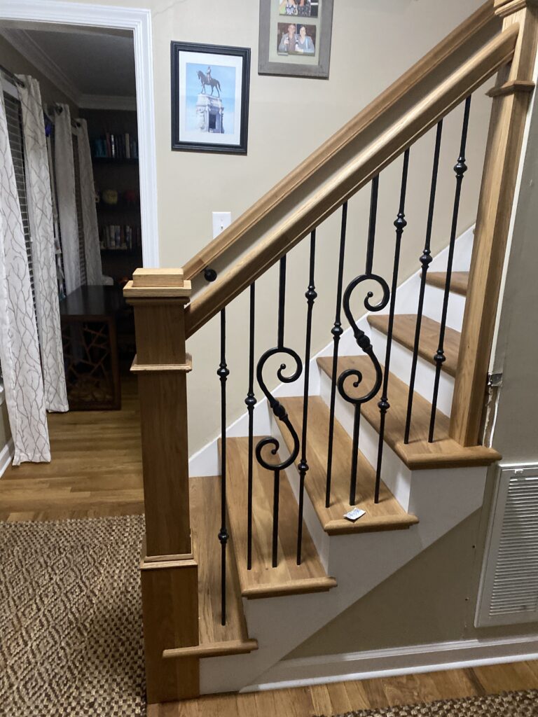 Wooden staircase with decorative black iron balusters.