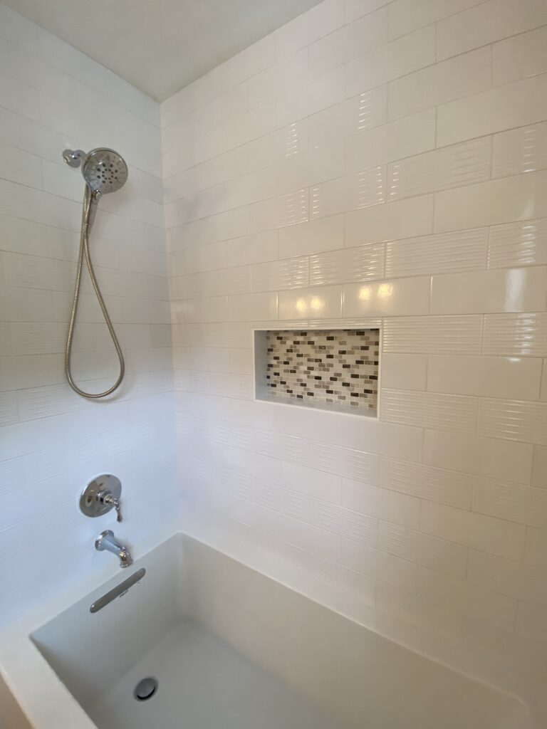 White tiled shower with built-in shelf.