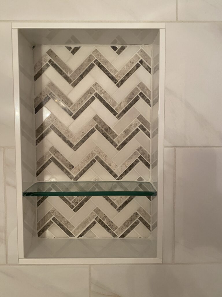 Chevron tile shower niche with glass shelf.