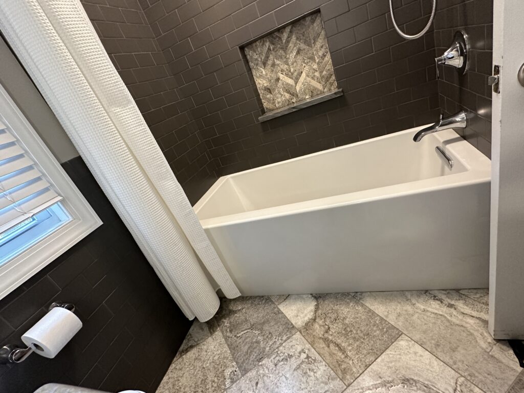 Modern bathroom with bathtub and dark tiles.
