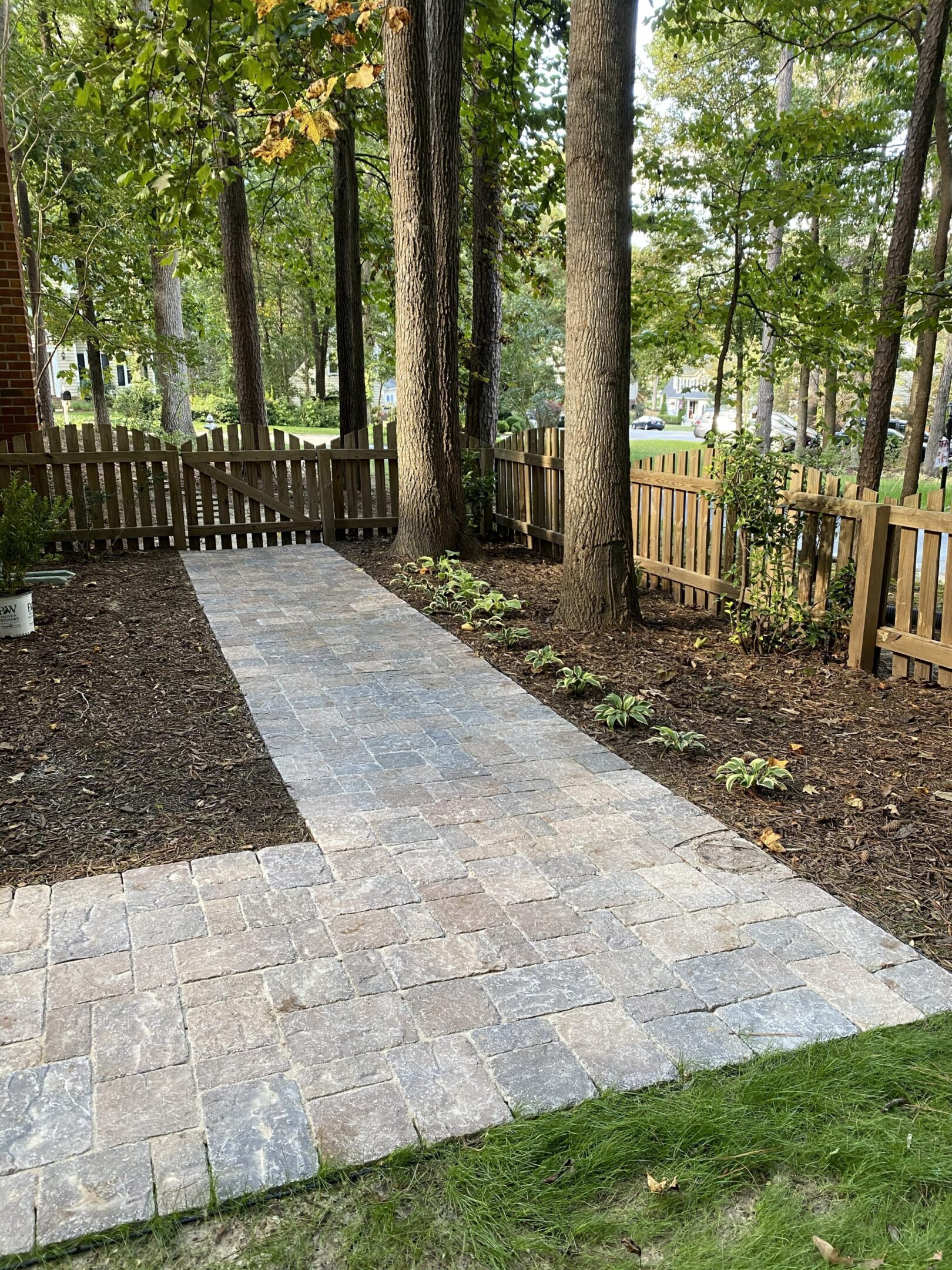 Brick pathway beside fenced wooded backyard.