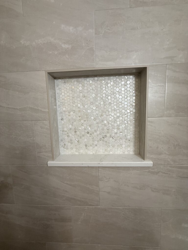 Recessed shower shelf with mosaic tile background.
