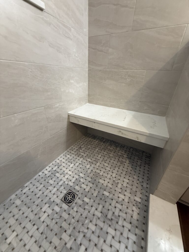 Shower with tiled floor and corner bench.