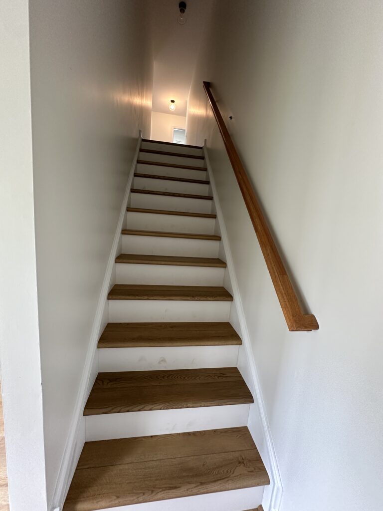 Wooden staircase with white walls and railing.