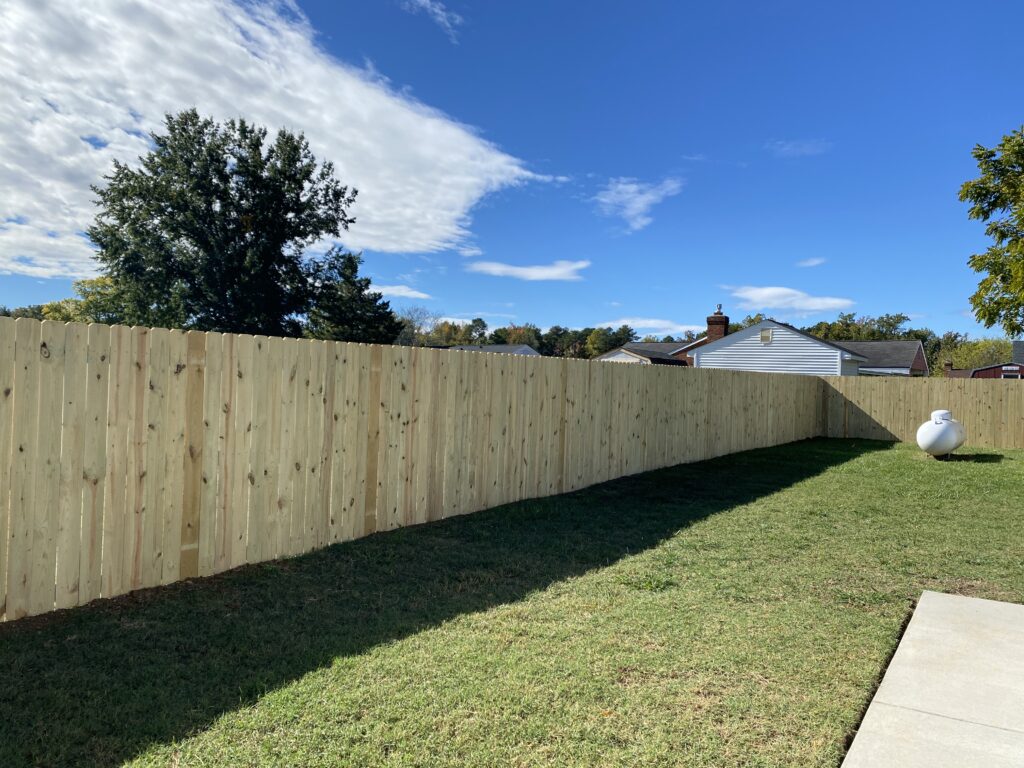 Wooden fence bordering grassy backyard, clear sky.