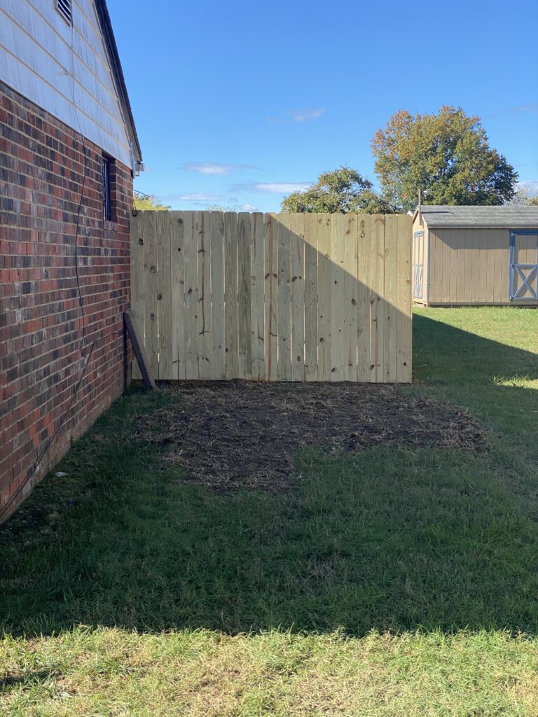 Wooden fence beside brick building and grass.